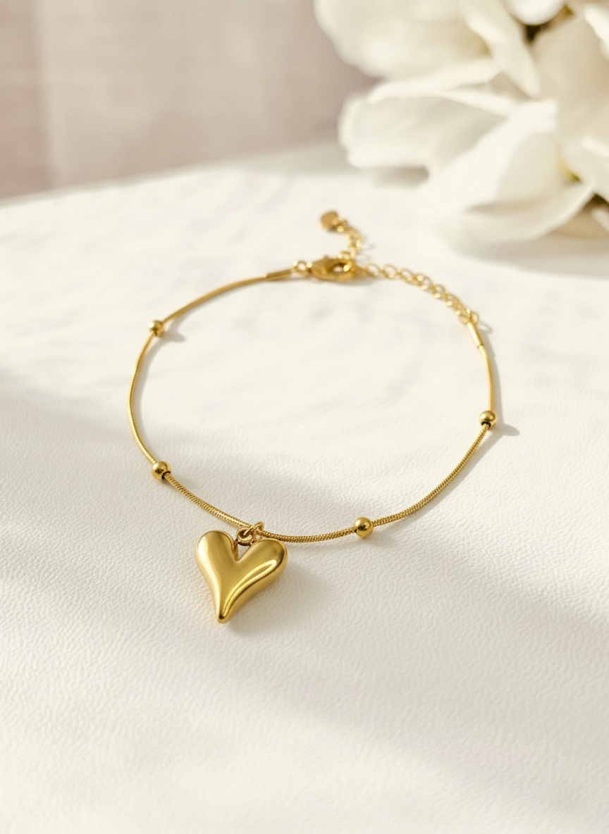 Gold bracelet with a heart charm on a white surface